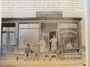 Black-and-white photo of seven people posed outside Dennison & Dillingham Meat Market and Groceries storefront.