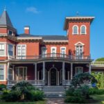 A large red Victorian-style house with a tower and wraparound porch, perfect for autumn in Maine, set against a blue sky.
