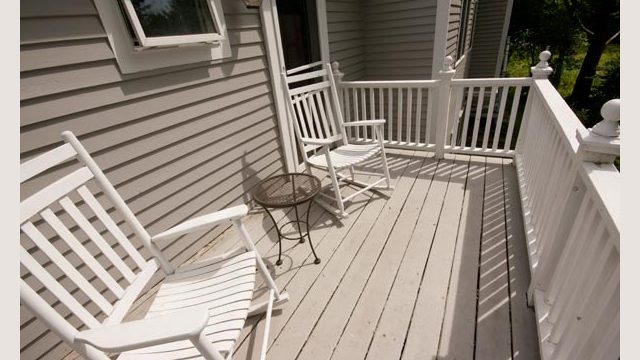 Two white rocking chairs and a small round table on a wooden porch with white railing.