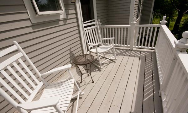 Two white rocking chairs and a small round table on a wooden porch with white railing.