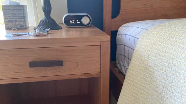 A wooden bed and nightstand with a Tiffany-style lamp, digital clock, and a yellow quilt on the bed.