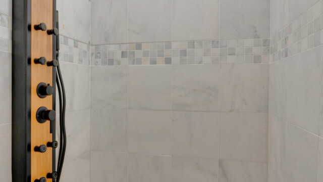 Modern shower with a rainfall showerhead, tile walls, and a wooden panel with control knobs. Hexagonal floor tiles.